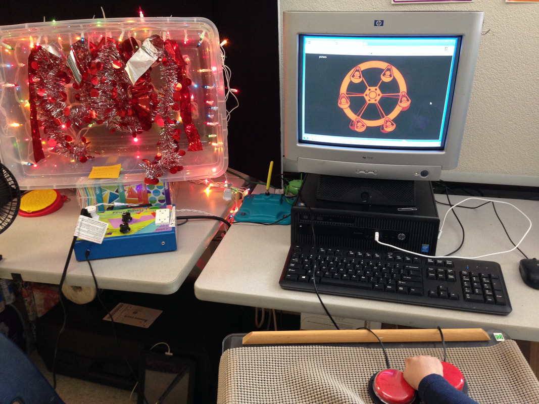 Picture of a sensory area using a clear box with lights and a tinsel garland suspended inside. Power Select box and switches to activate box and HelpKidzLearn game on switch activated computer.